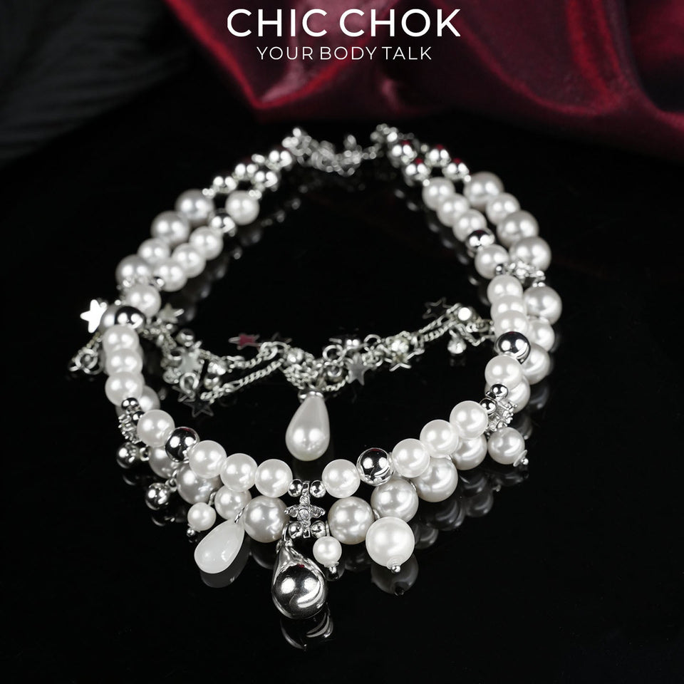 Fractured Cloud necklace with white beads, silver-colored chains and star-shaped charms on a dark background